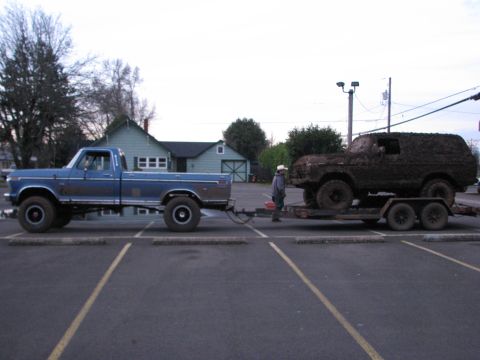 1978 Ford Bronco - A blue 1978 Ford pickup truck tows a mud-caked 1978 Ford Bronco on a trailer.