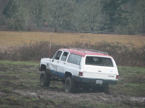 1978 Ford Bronco - This lifted SUV navigates a muddy terrain, its two-tone paint scheme contrasting with the wet environment.