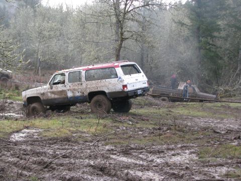 1978 Ford Bronco - Two vehicles struggle in the mud, with one SUV being pulled by a pickup truck in a wooded area.