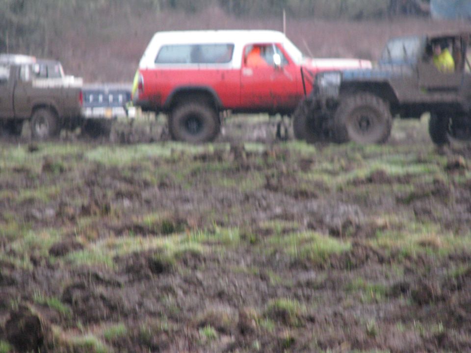 Red and white SUV with a trailer being towed by a brown pickup truck in a muddy field