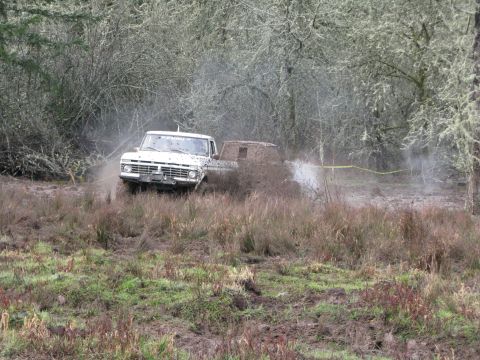 1978 Ford Bronco - A white pickup truck navigates a muddy off-road course, kicking up spray.