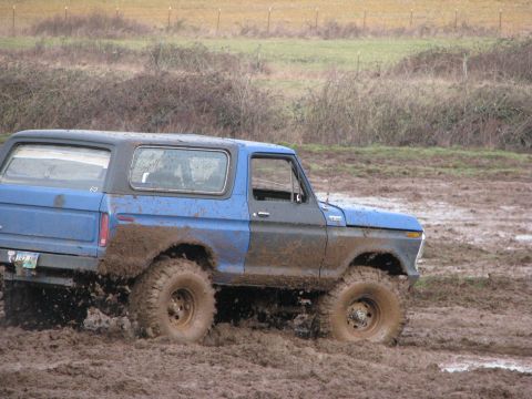 1978 Ford Bronco - A blue and gray 1978 Ford Bronco navigates a muddy terrain, kicking up dirt.