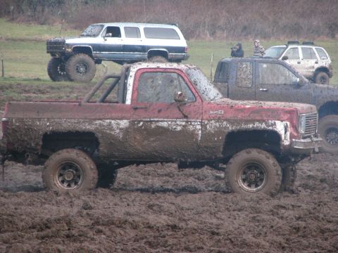1978 Ford Bronco - A red GMC pickup truck is stuck in the mud, with other vehicles visible in the background.
