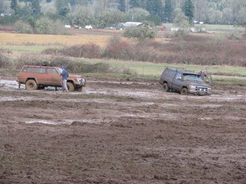 1978 Ford Bronco - Two SUVs are stuck in a muddy field, with one person standing near the red SUV.