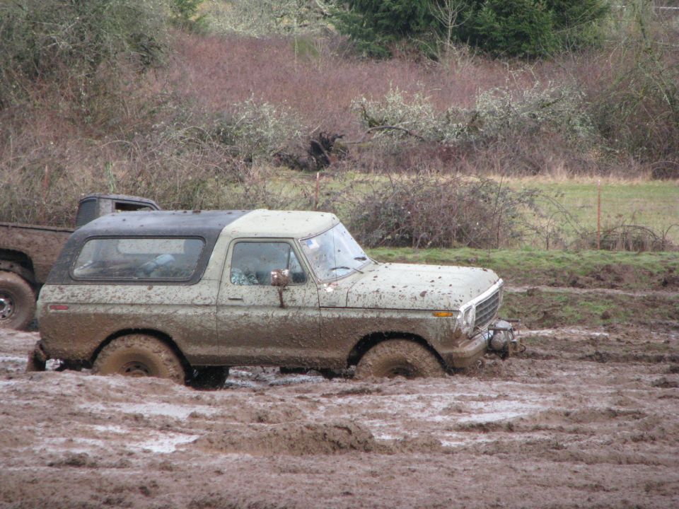 Muddy 1978 Ford Bronco stuck in a muddy field, with another truck partially visible behind it
