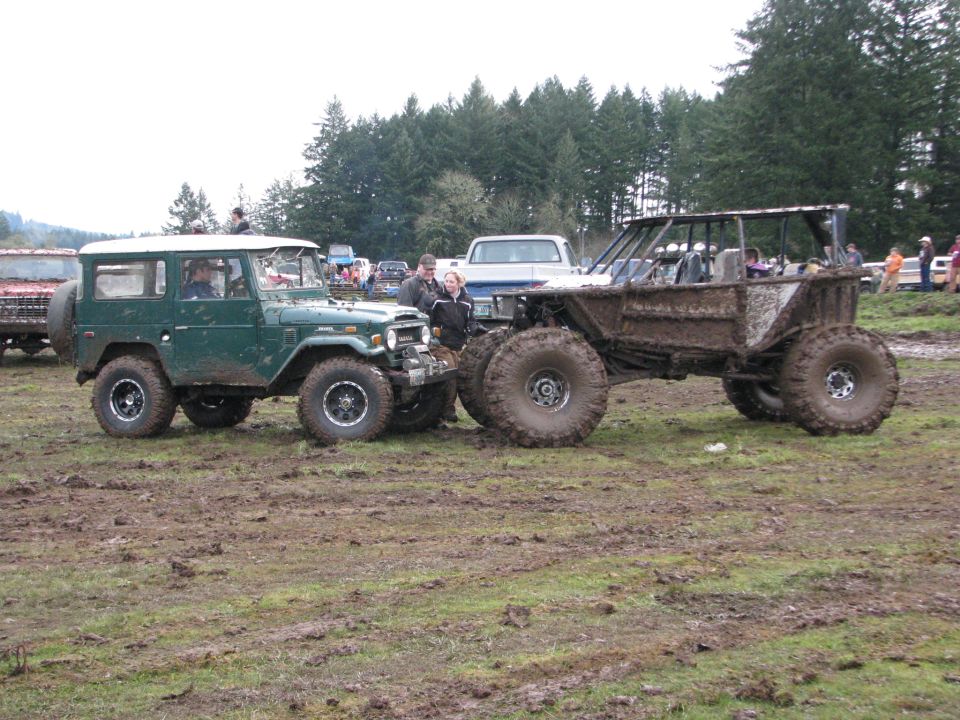 Green Toyota Land Cruiser FJ40 with a white hardtop and a custom mud bogger on large tires, both covered in mud
