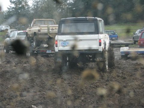 1978 Ford Bronco - A white Ford Bronco navigates a muddy track, with a pickup truck on a trailer behind it.
