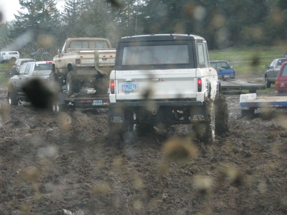 White Ford Bronco stuck in mud, towing a trailer with a pickup truck