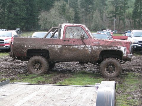 1978 Ford Bronco - A heavily muddied pickup truck sits in a muddy field, with other vehicles visible in the background.