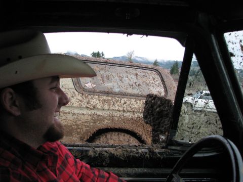 1978 Ford Bronco - Two off-road vehicles are stuck in deep mud, with a man in a cowboy hat observing.