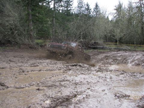 1978 Ford Bronco - A red SUV navigates a challenging muddy terrain, kicking up dirt as it goes.