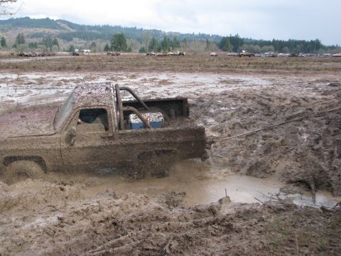 1978 Ford Bronco - A heavily mud-caked pickup truck is stuck in a muddy field, with other vehicles in the distance.