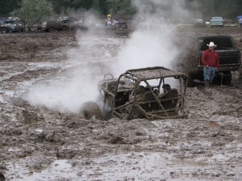 1978 Ford Bronco - An off-road buggy struggles for traction in a muddy track, while spectators watch from nearby vehicles.