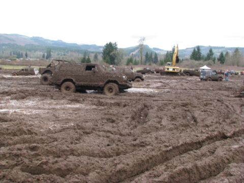 1978 Ford Bronco - Multiple off-road vehicles are covered in mud at an event, with an excavator visible in the distance.