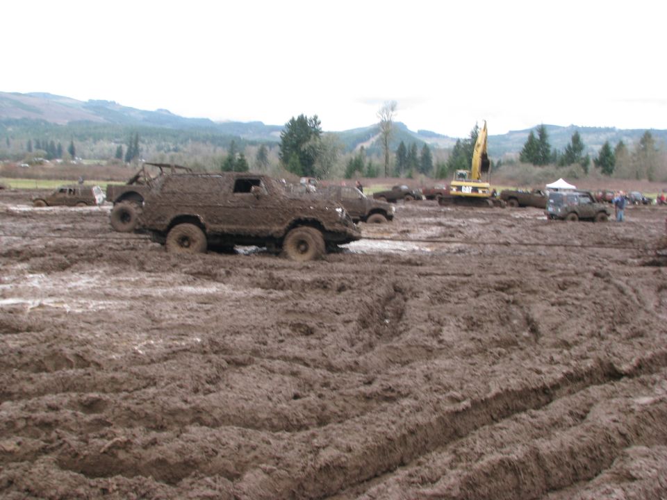 Muddy off-road vehicles stuck in a muddy field with a yellow excavator in the background