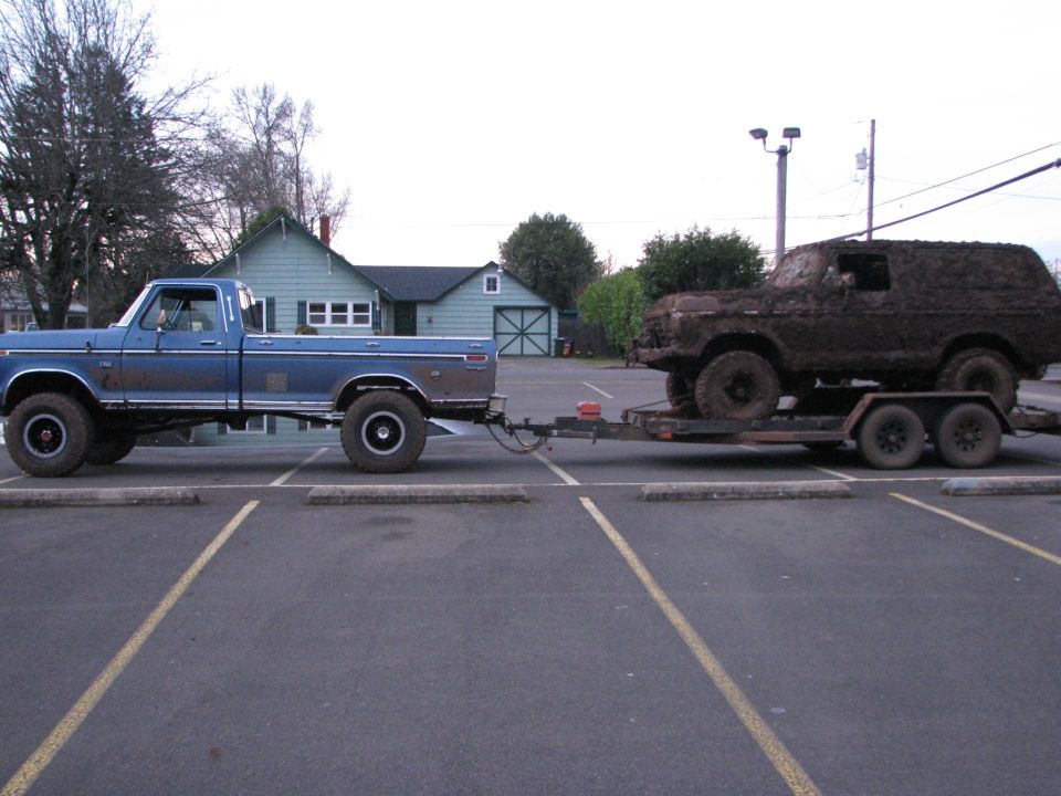 Blue pickup truck towing a trailer with a mud-covered SUV on it