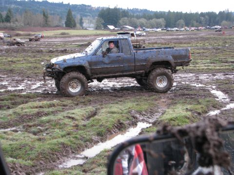1978 Ford Bronco - A blue pickup truck navigates a muddy off-road course, with other vehicles visible in the background.
