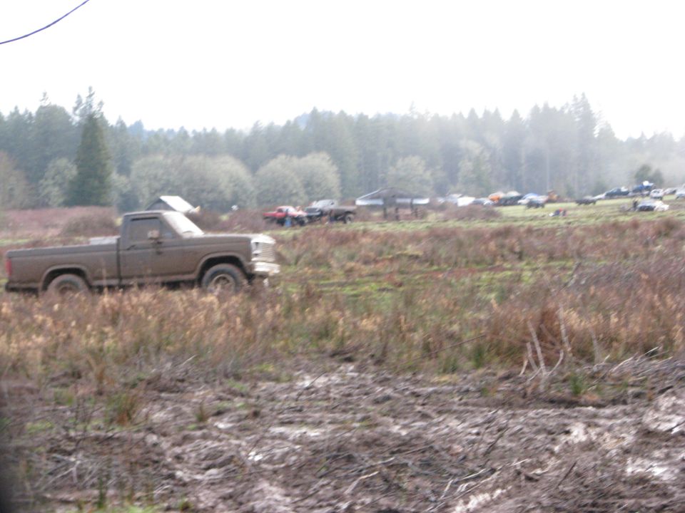 Muddy pickup truck parked in a field with other vehicles in the background