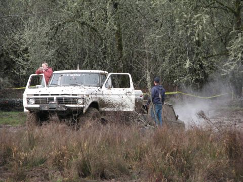 1978 Ford Bronco - Two vehicles are stuck in the mud during an off-road event, with spectators watching.