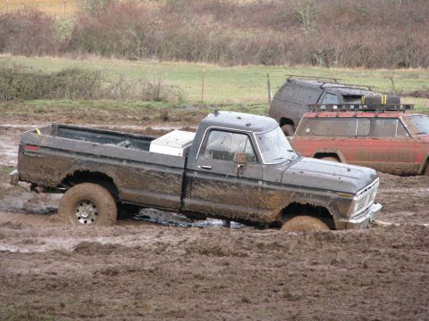 1978 Ford Bronco - A muddy black pickup truck is stuck in a muddy field, with two other vehicles visible in the background.