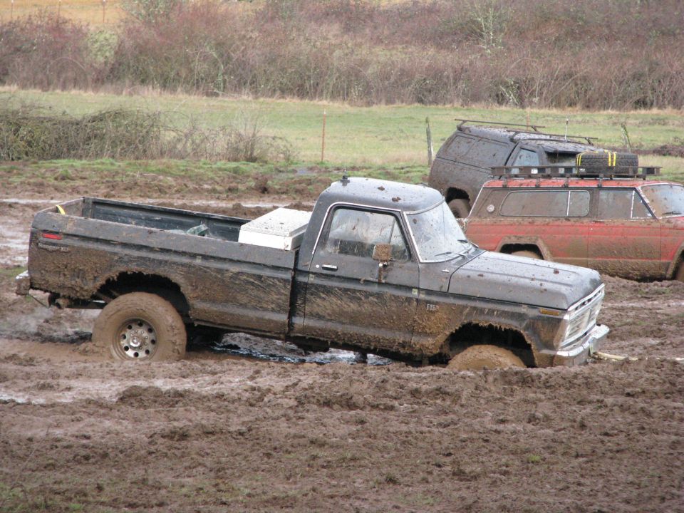 Muddy black pickup truck stuck in mud, with other vehicles behind