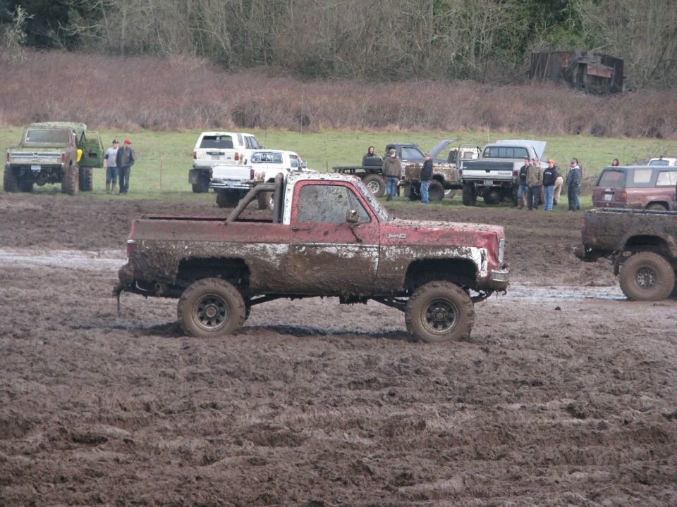 Mud-covered red and white pickup truck with roll bar, seen from the side