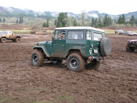 1978 Ford Bronco - A green Toyota Land Cruiser FJ40 navigates a muddy terrain with other vehicles in the background.