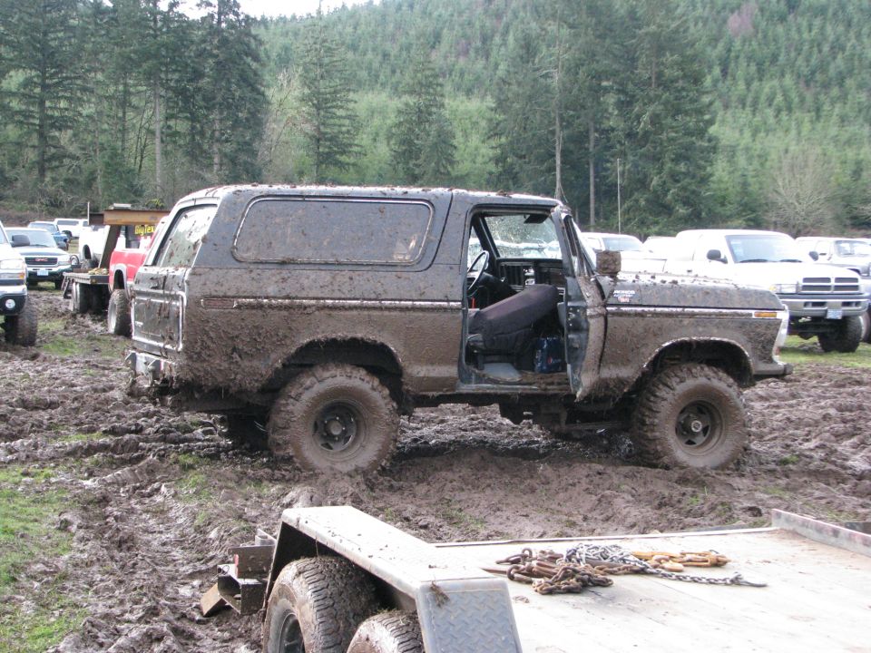 Muddy 1978 Ford Bronco with door open, parked in a muddy field with other vehicles around