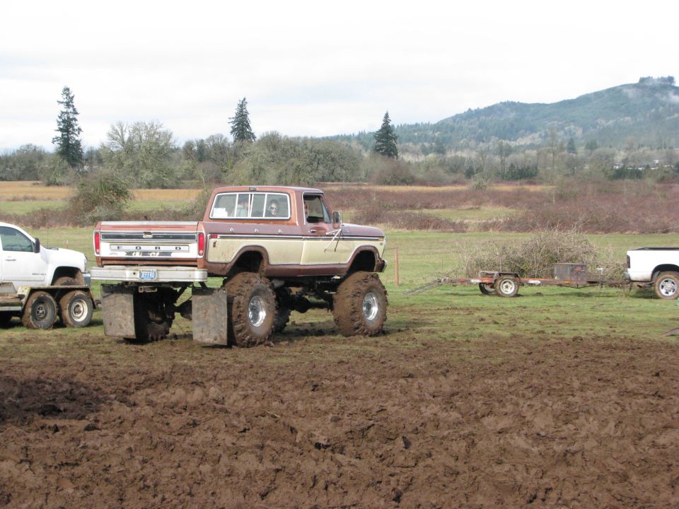Brown and tan Ford pickup truck with large tires, towing a trailer in mud