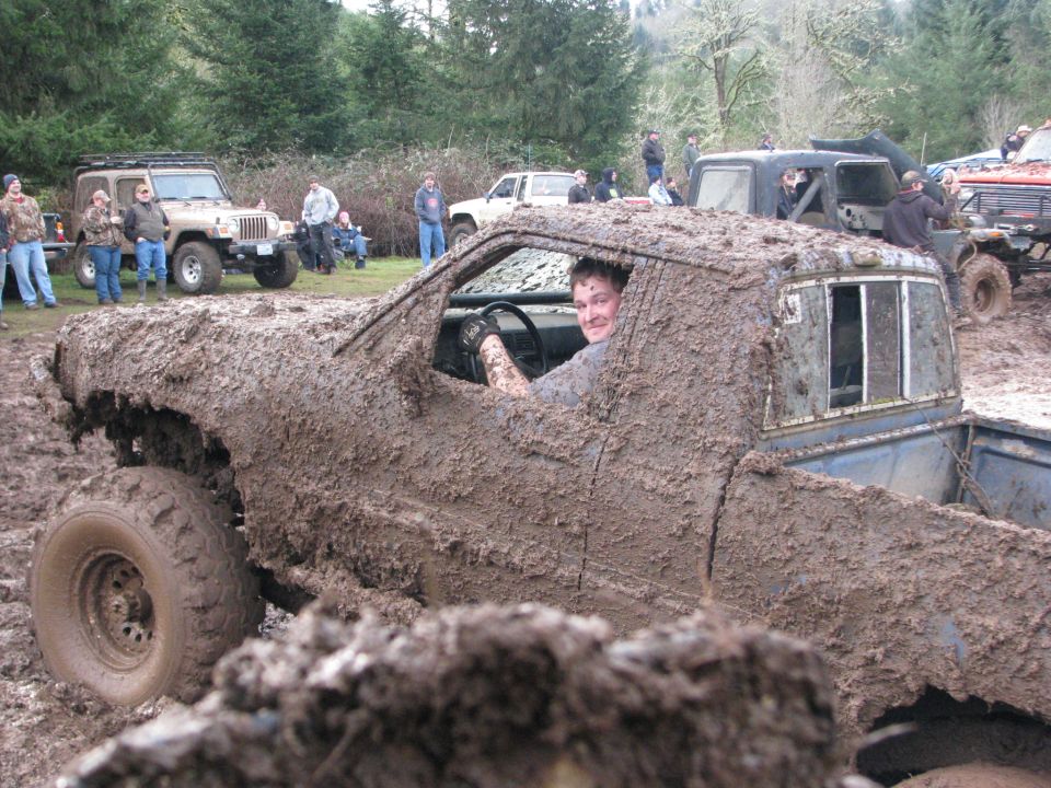Mud-covered pickup truck with driver, other off-road vehicles in background