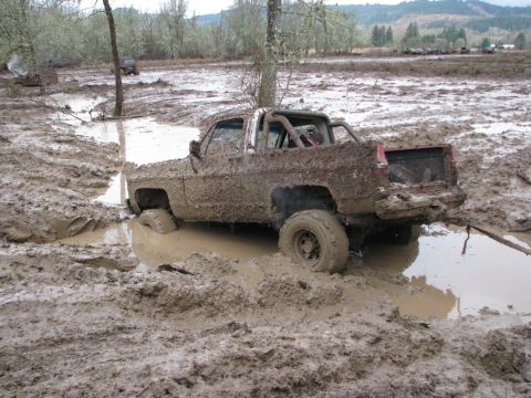 1978 Ford Bronco - A heavily mud-covered pickup truck is stuck in a muddy field, with other vehicles visible in the distance.