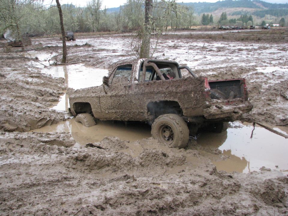 Mud-covered pickup truck stuck in mud, with other vehicles in background
