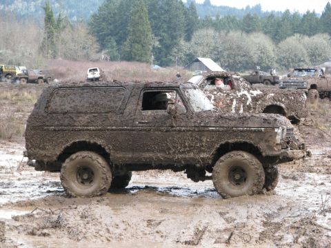 1978 Ford Bronco - Several off-road vehicles are covered in mud during an event, with one SUV prominently featured in the foreground.
