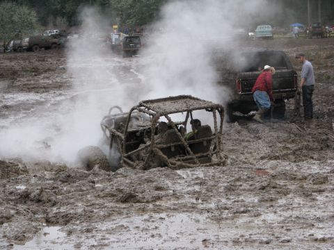1978 Ford Bronco - An off-road buggy is stuck in thick mud, surrounded by other vehicles and onlookers in a muddy terrain.