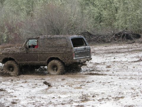 1978 Ford Bronco - A 1978 Ford Bronco navigates a challenging muddy terrain, kicking up spray as it drives.