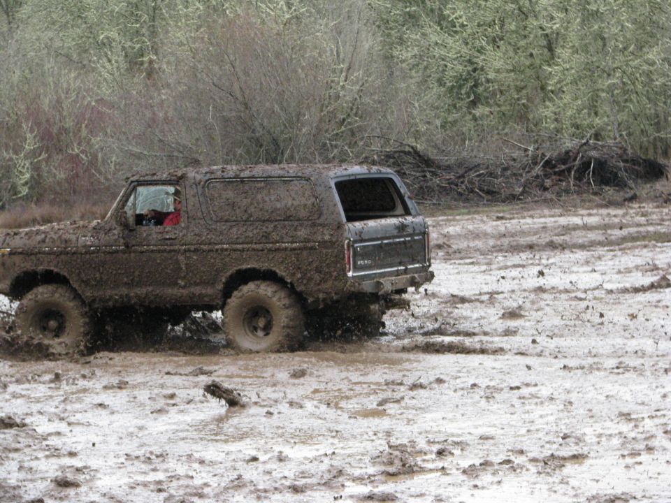 Mud-covered 1978 Ford Bronco driving through a muddy field