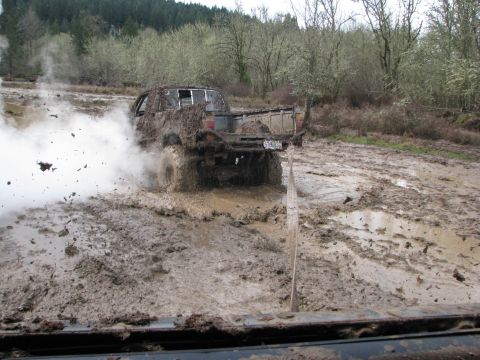 1978 Ford Bronco - Pickup truck stuck in a mud bog, tires spinning and throwing mud.