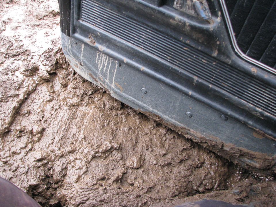 Close-up of a vehicle's side panel and running board deep in thick mud