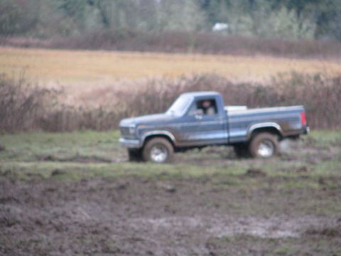 1978 Ford Bronco - A blue pickup truck navigates a muddy field, appearing to be from the 1979 model year.