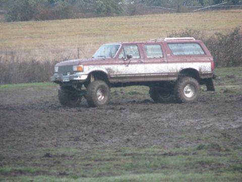 1978 Ford Bronco - Modified four-door SUV navigating a muddy field, likely a Ford Bronco from the early 1990s.