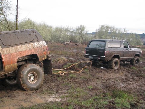 1978 Ford Bronco - A black 1978 Ford Bronco is being pulled out of the mud by another vehicle in a field.