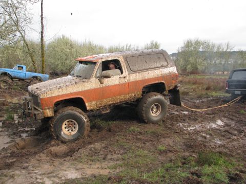 1978 Ford Bronco - An orange and white SUV is stuck in the mud, with a blue pickup truck nearby and another vehicle being towed out.
