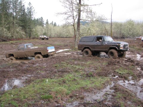 1978 Ford Bronco - A 1978 Ford Bronco tackles a challenging muddy terrain, while a pickup truck appears stuck in the mire.