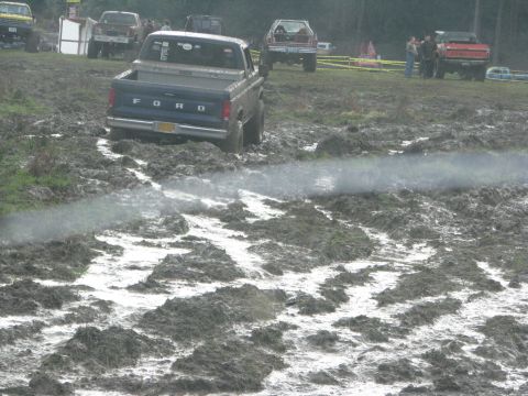 1978 Ford Bronco - Multiple trucks navigate a muddy off-road course during an event.
