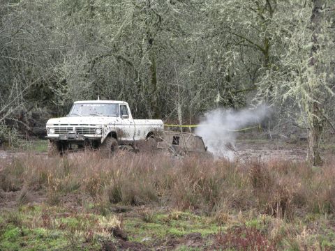 1978 Ford Bronco - A muddy white pickup truck is stuck in a field, with smoke billowing from its exhaust pipe.