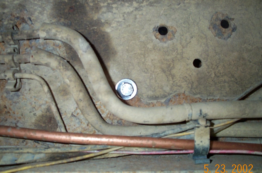 Exhaust pipe routed over a rusty frame rail with new bolt, copper line and wiring