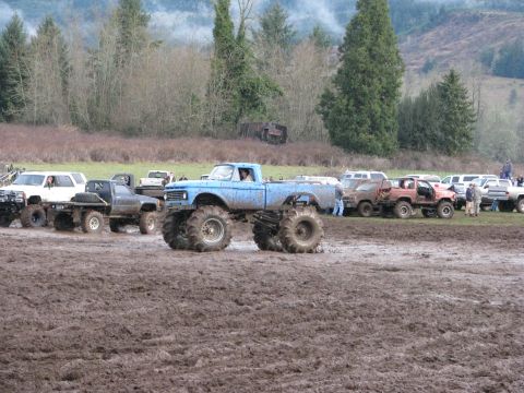1978 Ford Bronco - Several trucks are gathered in a muddy area, with trees and hills in the distance.