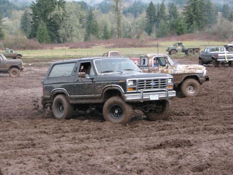 1978 Ford Bronco - Multiple off-road vehicles navigate a muddy terrain under overcast skies.