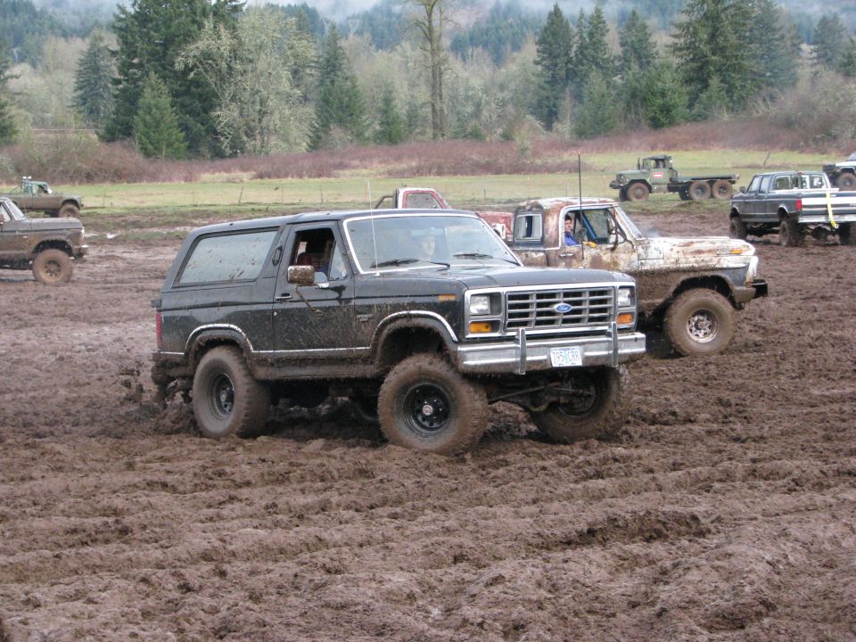 Black Ford Bronco with lifted suspension driving through mud, front grille visible