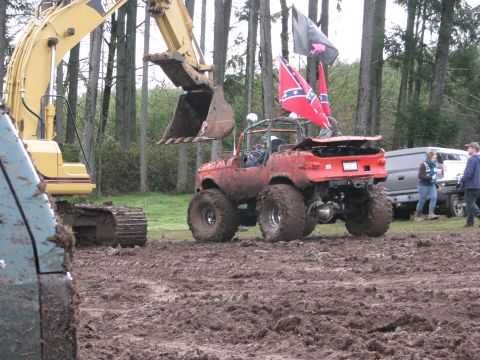 1978 Ford Bronco - Muddy off-road vehicle with flags, next to an excavator and a van in a wooded area.